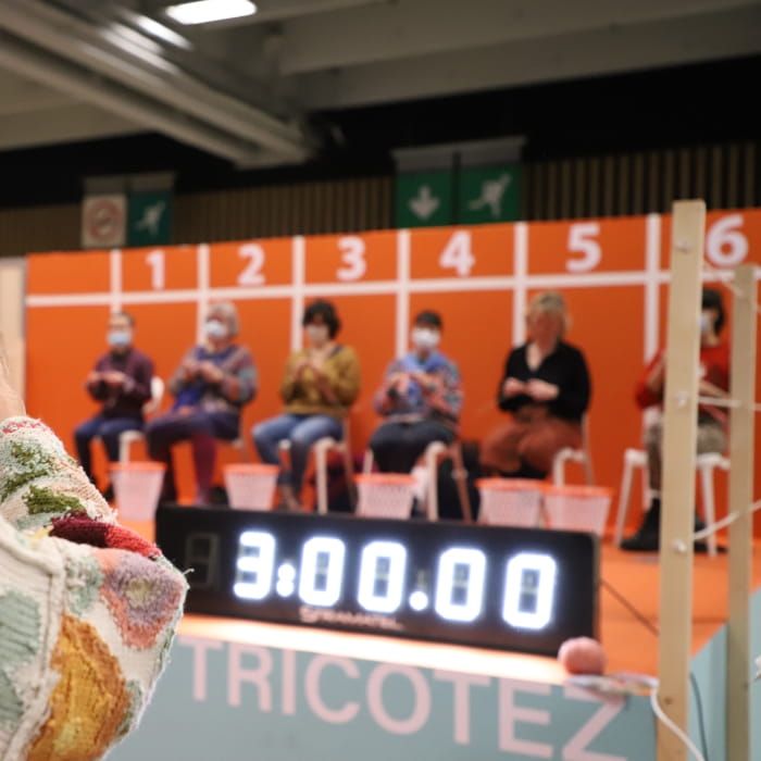 groupe de personnes assises pour un concours de rapidité de tricot avec un chronomètre